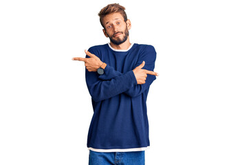Handsome blond man with beard wearing casual sweater pointing to both sides with fingers, different direction disagree