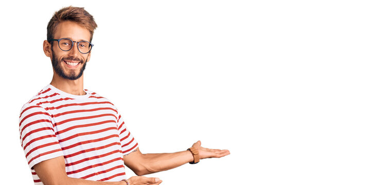 Handsome blond man with beard wearing casual clothes and glasses inviting to enter smiling natural with open hand