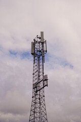 Tower with 5G and 4G cellular network antenna on blue cloudy sky background.
