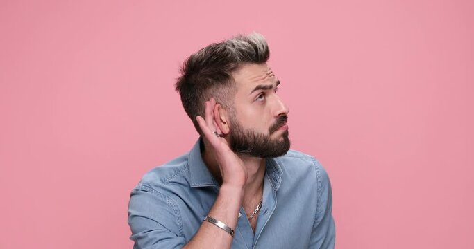 attractive casual man gesturing I can't hear you and bla bla bla on pink background