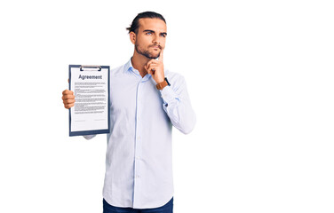 Young handsome man holding clipboard with agreement document serious face thinking about question...