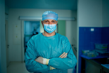 Fototapeta na wymiar Doctor stands cross hands. Blue scrubs. Hospital medical hall background.