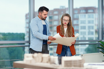 Experienced bearded male designer and his female colleague with dreadlocks analysing blueprints of future project.