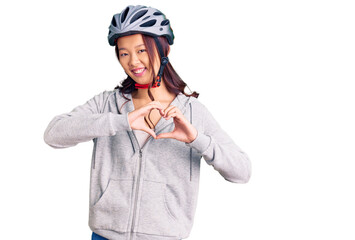 Young beautiful chinese girl wearing bike helmet smiling in love showing heart symbol and shape with hands. romantic concept.