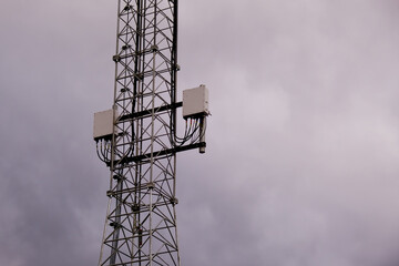 Detail of tower with 5G and 4G cellular network antenna on grey cloudy sky background.