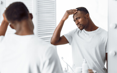 Black Guy Examining His Head Searching Gray Hair In Bathroom - obrazy, fototapety, plakaty