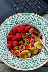 Eating an acai bowl with fresh figs, raspberries, banana and granola while working on a laptop computer
