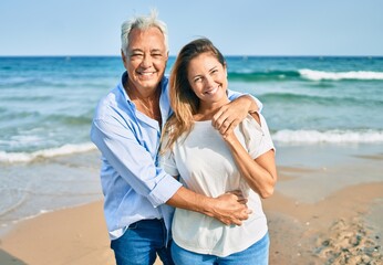 Fototapeta na wymiar Middle age hispanic couple smiling happy and hugging walking at the beach