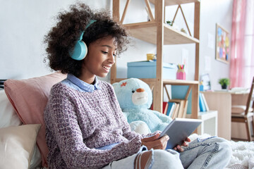 Happy african kid girl holding digital tablet elearning at home. Smiling mixed race school child...