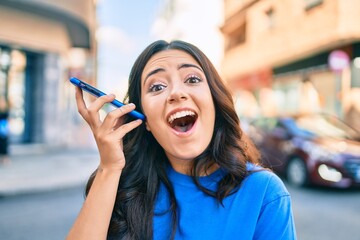 Young hispanic woman smiling happy listening audio message using smartphone at the city.