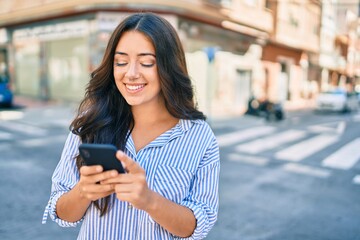 Fototapeta premium Young hispanic businesswoman smiling happy using smartphone at the city.