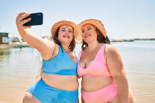 Two plus size overweight sisters twins women happy taking a selfie picture at the beach on summer holidays