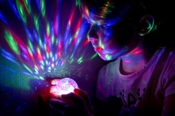 Fototapeta na wymiar Little girl holding a glowing ball with colorful lights in her hands