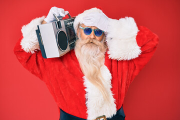 Old senior man wearing santa claus costume and boombox stressed and frustrated with hand on head, surprised and angry face
