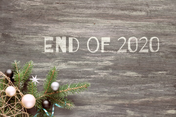 Text End of 2020. Top view on dark wood with corner decorated fir twigs and silver toys.