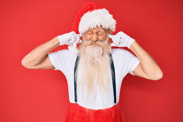 Old senior man with grey hair and long beard wearing white t-shirt and santa claus costume covering...