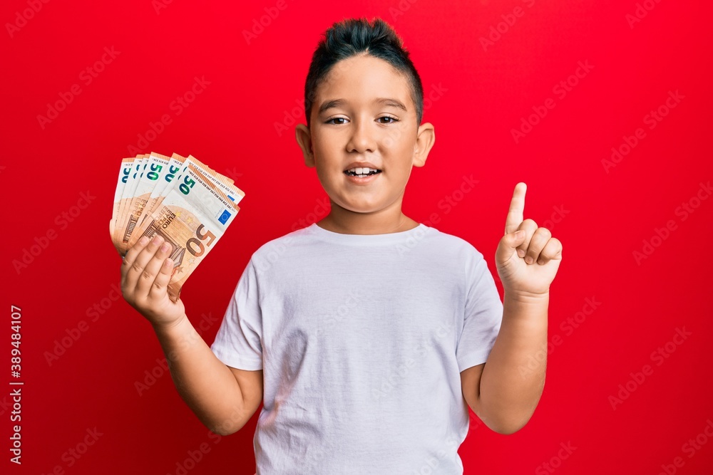 Canvas Prints Little boy hispanic kid holding bunch of 50 euro banknotes smiling with an idea or question pointing finger with happy face, number one