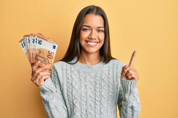 Beautiful hispanic woman holding bunch of 50 euro banknotes smiling happy pointing with hand and...