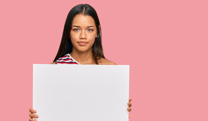 Beautiful hispanic woman holding blank empty banner thinking attitude and sober expression looking self confident