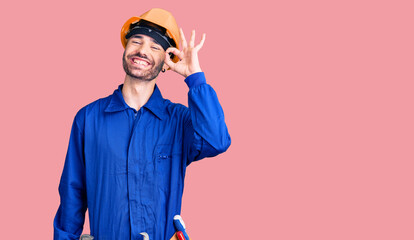 Young hispanic man wearing worker uniform smiling positive doing ok sign with hand and fingers. successful expression.