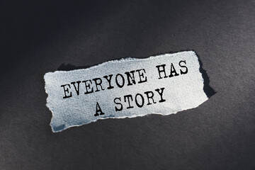 Everyone has a story - text on torn paper on dark desk in sunlight.