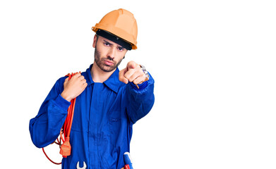 Young hispanic man wearing elecrician uniform holding cable pointing with finger to the camera and to you, confident gesture looking serious