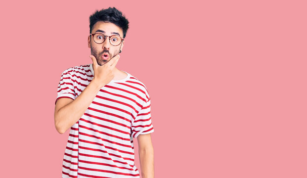 Young hispanic man wearing casual clothes looking fascinated with disbelief, surprise and amazed expression with hands on chin