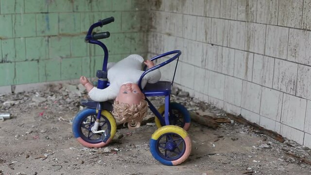 Baby tricycle with a doll stands in an abandoned building.