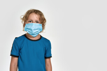 Portrait of little sportive boy child in sportswear wearing medical mask, looking at camera while posing, standing isolated over white background