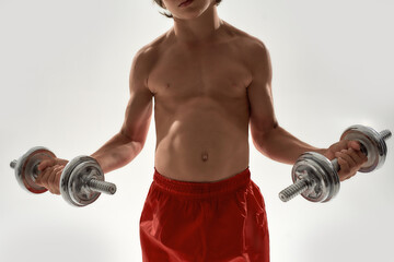 Cropped shot of little sportive boy child with muscular body lifting weights while standing...