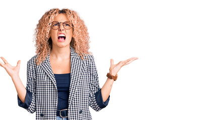 Young blonde woman with curly hair wearing business jacket and glasses crazy and mad shouting and...