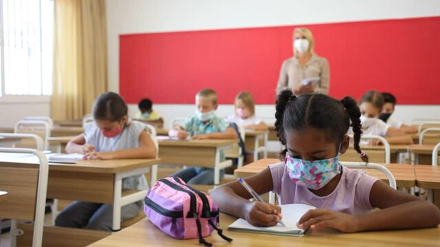 Portrait of focused schoolgirl wearing protective face mask working at lesson in classroom, writing exercise. High quality FullHD footage