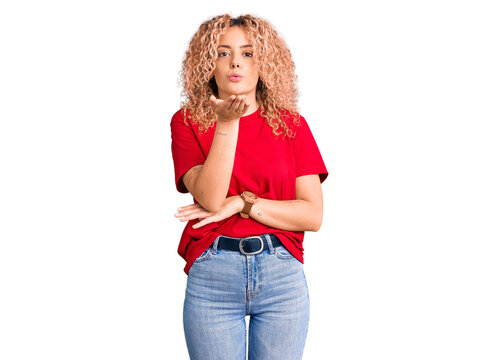 Young blonde woman with curly hair wearing casual red tshirt looking at the camera blowing a kiss with hand on air being lovely and sexy. love expression.