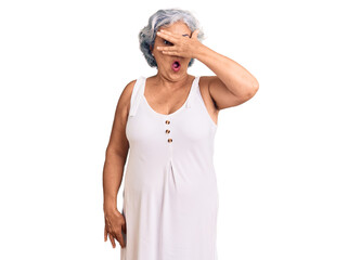 Senior woman with gray hair wearing casual clothes peeking in shock covering face and eyes with hand, looking through fingers with embarrassed expression.