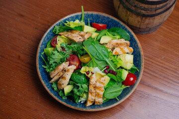 Grilled Chicken salad in white background, Grilled chicken, quinoa, pomegranate, mix leaves, kale, avocado, cherry tomato and cucumber with orange dressing.