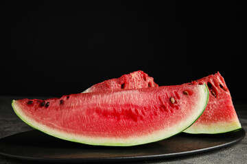 Yummy watermelon slices on grey table against black background