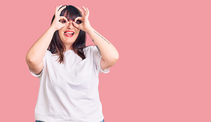 Young plus size woman wearing casual clothes doing ok gesture like binoculars sticking tongue out, eyes looking through fingers. crazy expression.