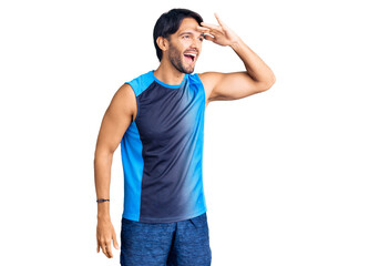Handsome hispanic man wearing sportswear very happy and smiling looking far away with hand over head. searching concept.