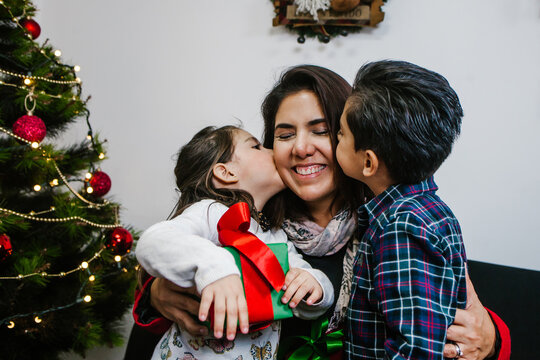 mexican son and daugther children kissing her mom on a Christmas decorated home