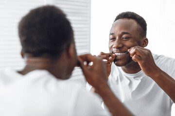 Toothy African Man Flossing Teeth Using Floss Standing In Bathroom