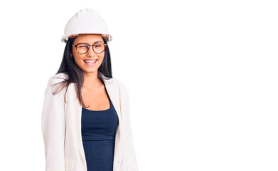 Young beautiful latin girl wearing architect hardhat and glasses winking looking at the camera with sexy expression, cheerful and happy face.