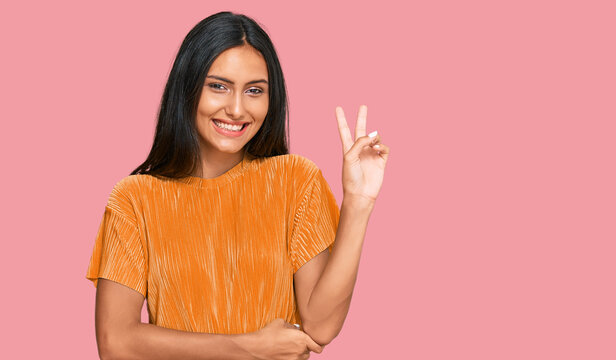 Young brunette arab woman wearing casual clothes smiling with happy face winking at the camera doing victory sign. number two.