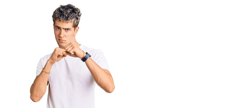 Young handsome man wearing casual white tshirt ready to fight with fist defense gesture, angry and upset face, afraid of problem
