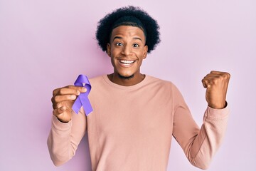 African american man with afro hair holding awareness purple ribbon screaming proud, celebrating...