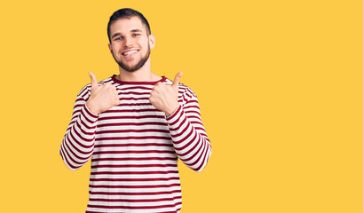 Young handsome man wearing striped sweater success sign doing positive gesture with hand, thumbs up smiling and happy. cheerful expression and winner gesture.