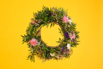 Wreath made of beautiful flowers hanging on yellow background