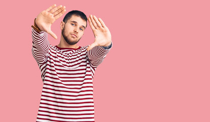 Young handsome man wearing striped sweater doing frame using hands palms and fingers, camera perspective