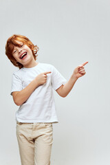 Cheerful red-haired boy shows his fingers to the side of a white T-shirt fun childhood 