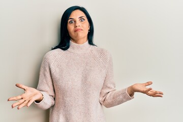 Young caucasian woman wearing casual winter sweater clueless and confused expression with arms and hands raised. doubt concept.