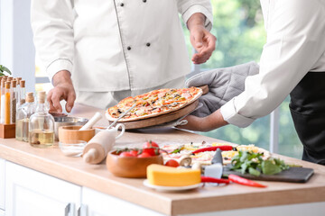 Mature chefs with tasty pizza in kitchen